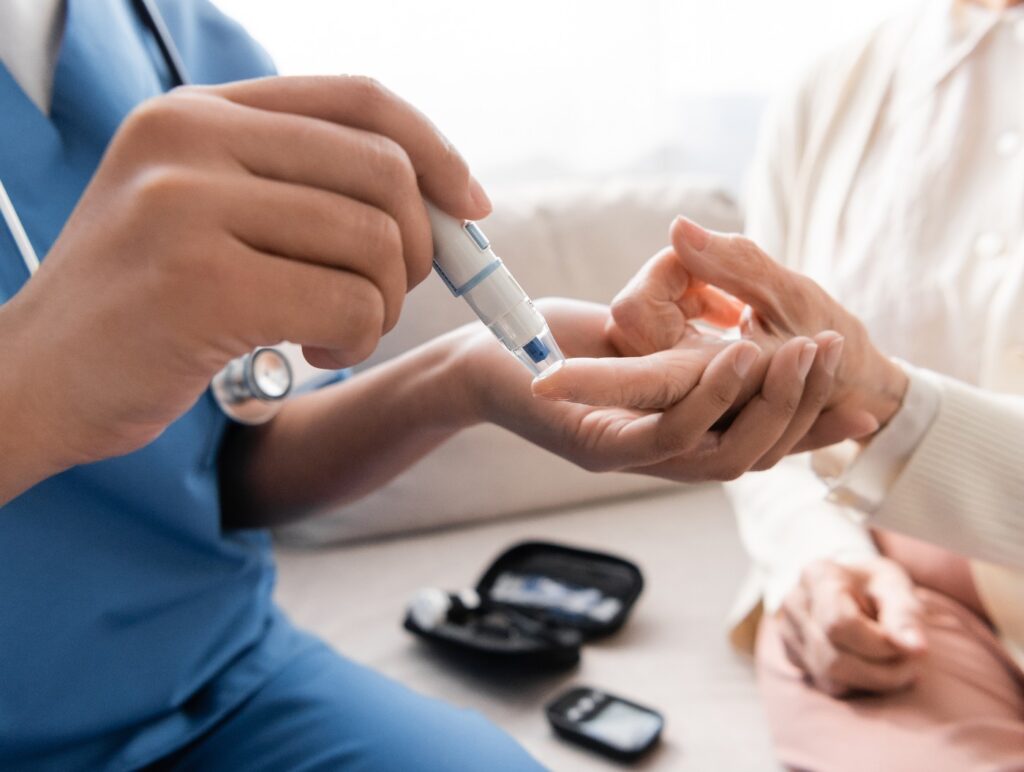 Ausschnitt einer multirassischen Krankenschwester, die einer älteren Frau mit einem Lanzettenstift eine Blutprobe entnimmt.