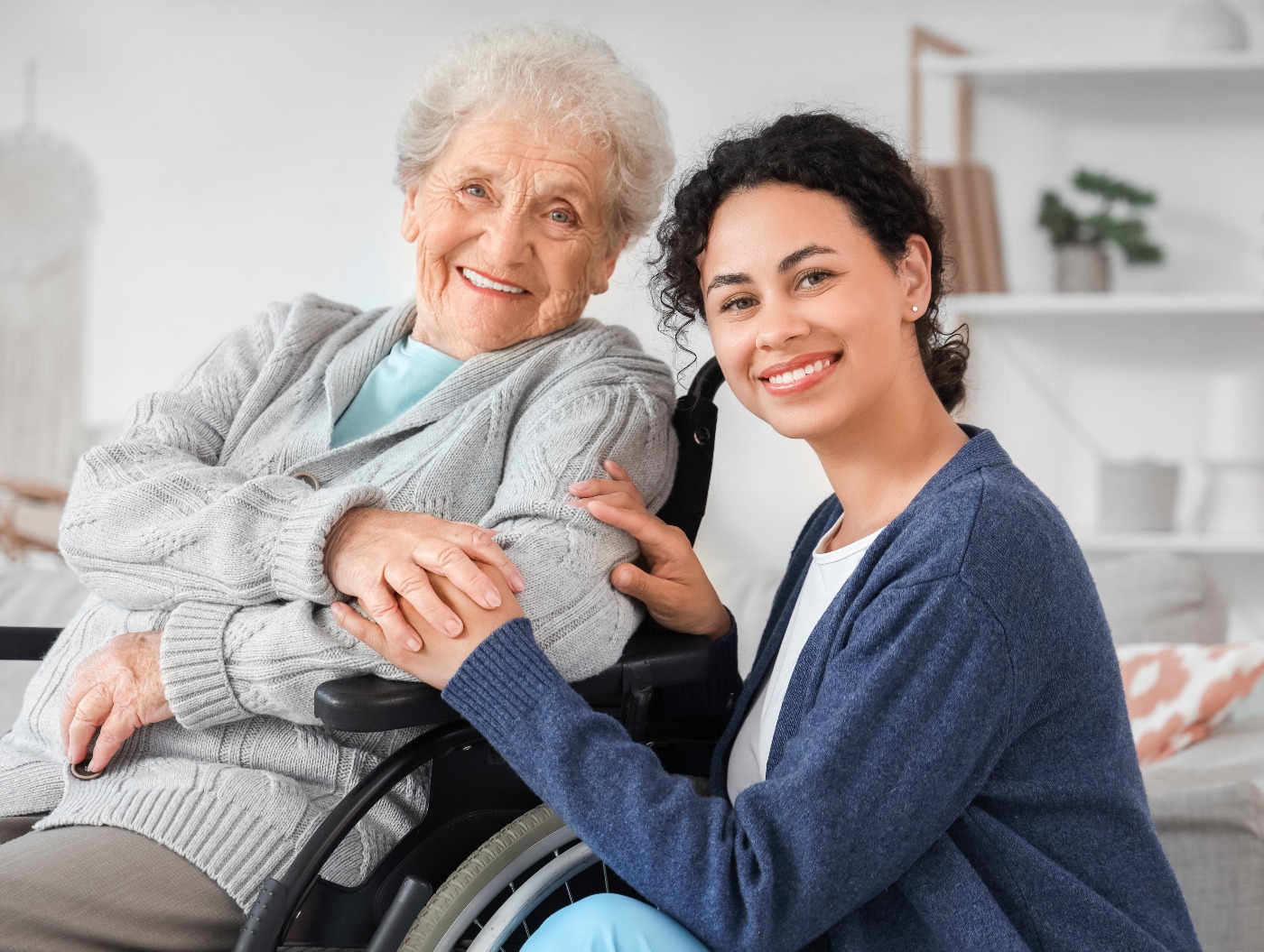 Junge afroamerikanische medizinische Mitarbeiterin mit älterer Frau im Rollstuhl in einem Pflegeheim